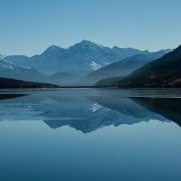 Mountain lake reflecting snow-capped peaks under blue sky